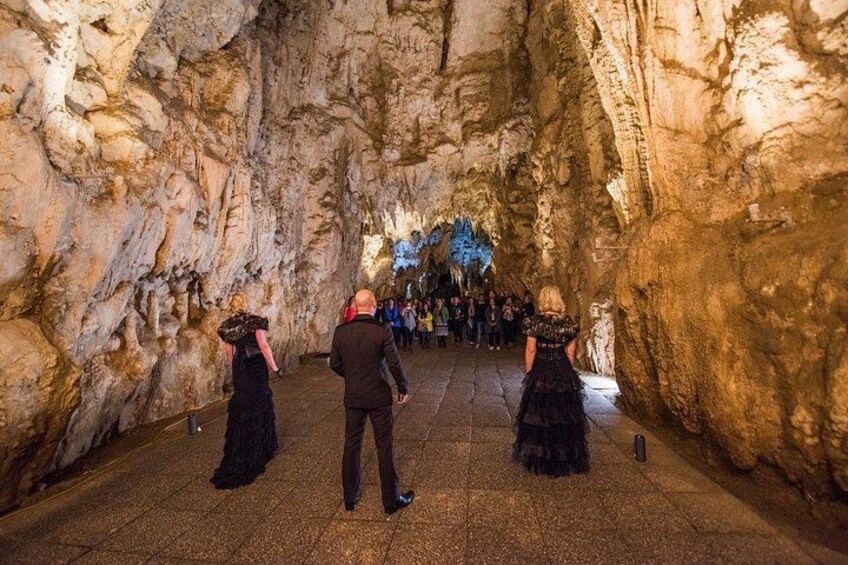 Un gruppo di persone cammina attraverso una grotta con pareti rocciose e un soffitto illuminato di blu. 3