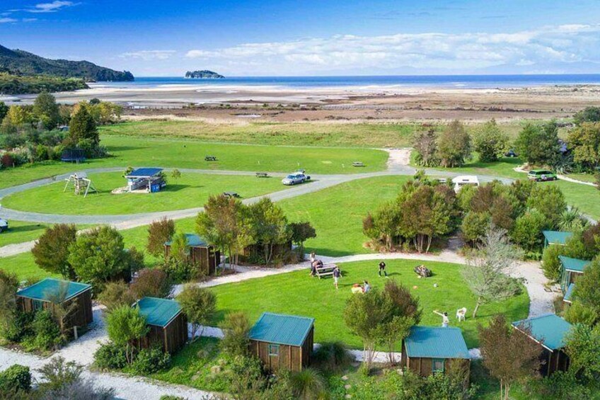 Un camping con cabañas, un campo cubierto de césped y una playa al fondo. 2