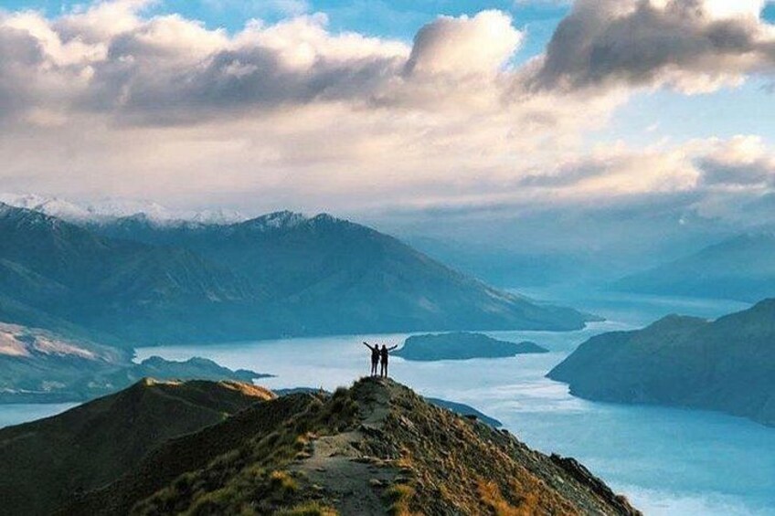 A mountainous landscape with a lake and two people standing on a ridge. 2