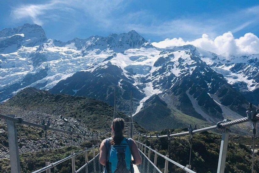 A person standing on a metal bridge with a mountainous landscape in the background. 1