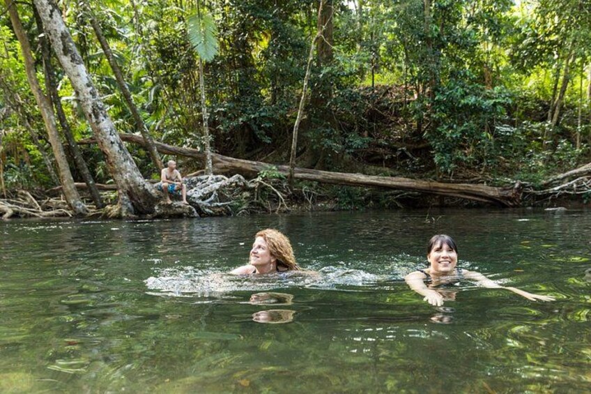Two people swimming in a river surrounded by dense forest. 2
