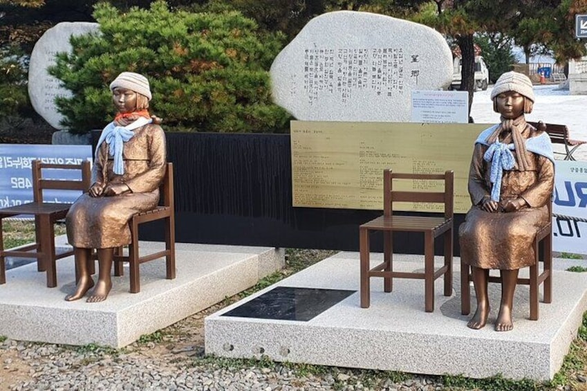 Two bronze statues of a seated woman with a scarf, placed on pedestals in a park. 3