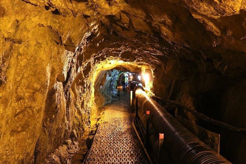 A tunnel with a metal walkway and a large pipe. 5