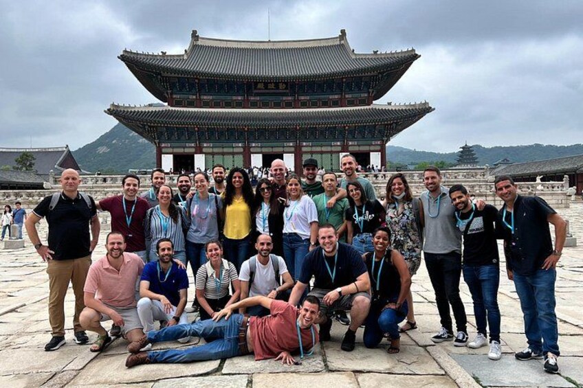 A group of people posing in front of a traditional Korean building with a tiled roof and multiple eaves. 2