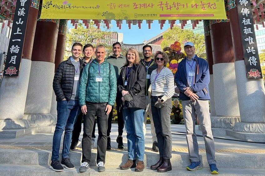A group of people standing under a traditional archway with floral decorations and a banner. 2