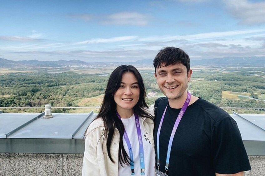 Dos personas de pie en una azotea con vistas a un paisaje verde y montañas a lo lejos. 2