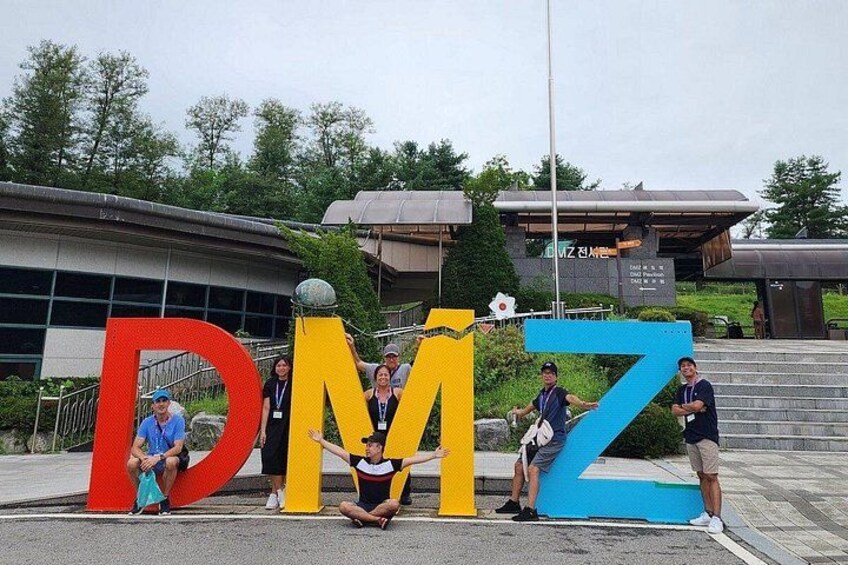 Un grupo de personas posando frente a grandes letras que deletrean 'DMZ'. 3