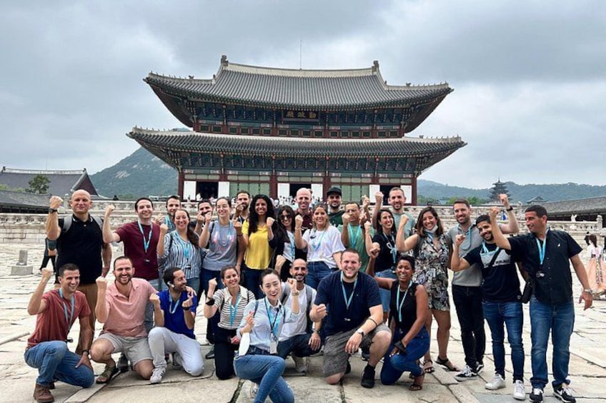 A group of people posing in front of a traditional Korean building with a tiled roof and wooden structure. 3