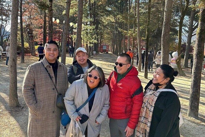 A group of people standing in a park with trees and a pathway. 4