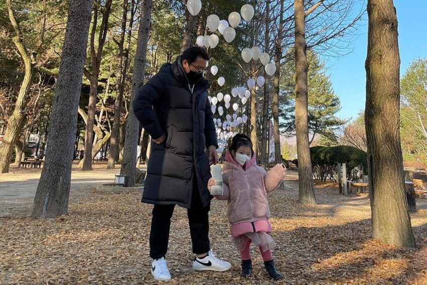 A person and a child in a park with trees and a clear sky. 3