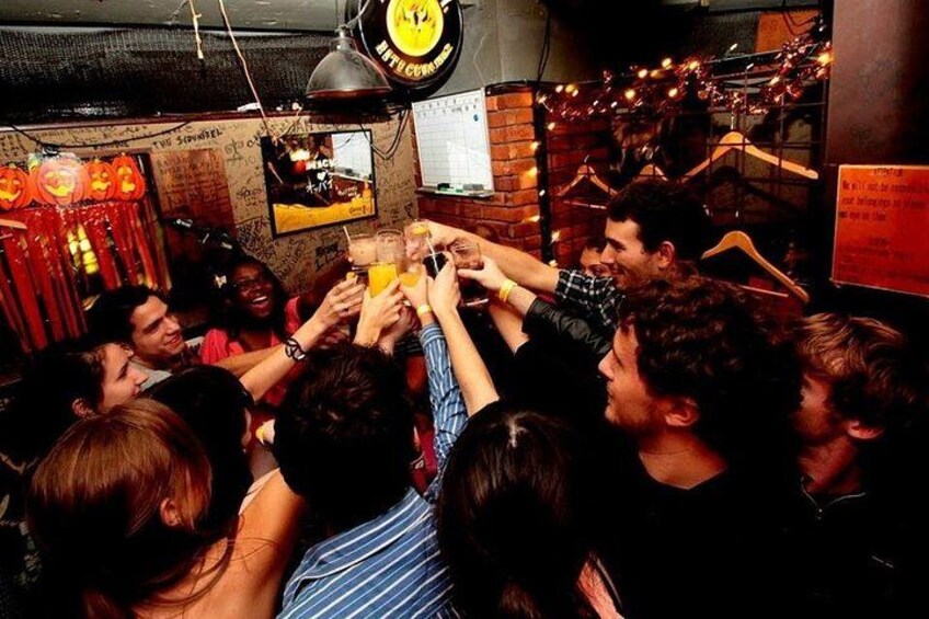 A group of people toasting with drinks in a dimly lit indoor setting with brick walls and festive decorations. 3