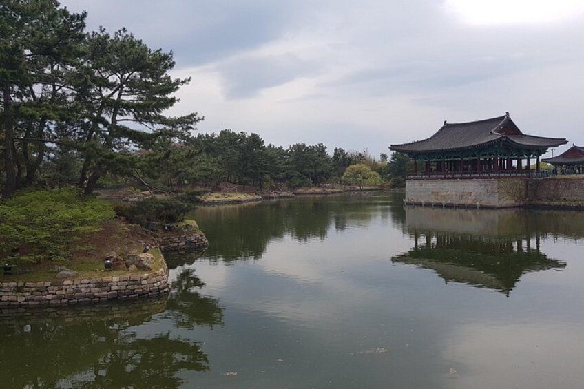 A calm lake with a traditional building reflecting on the water, surrounded by trees and a stone wall. 5