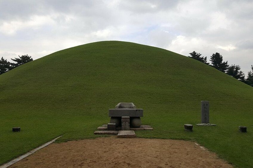 A mound with a stone structure at the top, surrounded by a grassy area and a dirt path leading to it. 4
