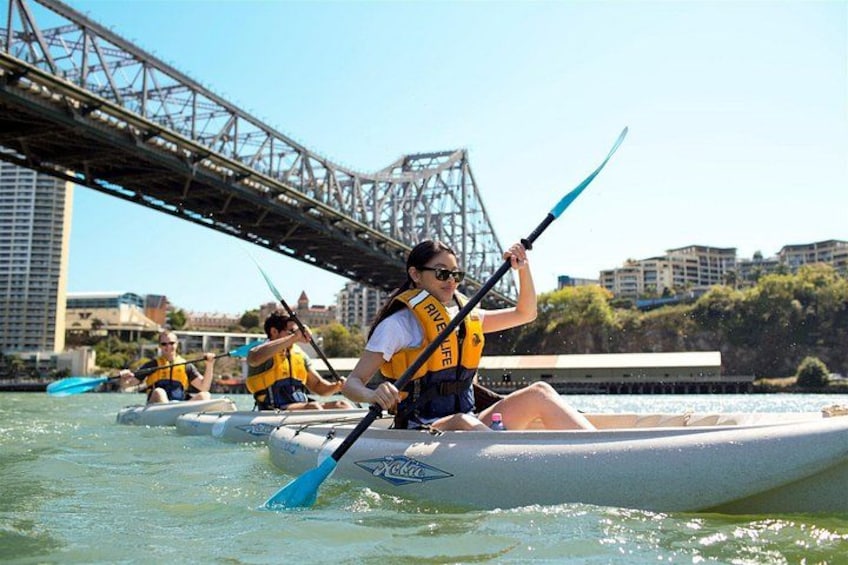 People kayaking on a river with a bridge in the background. 1