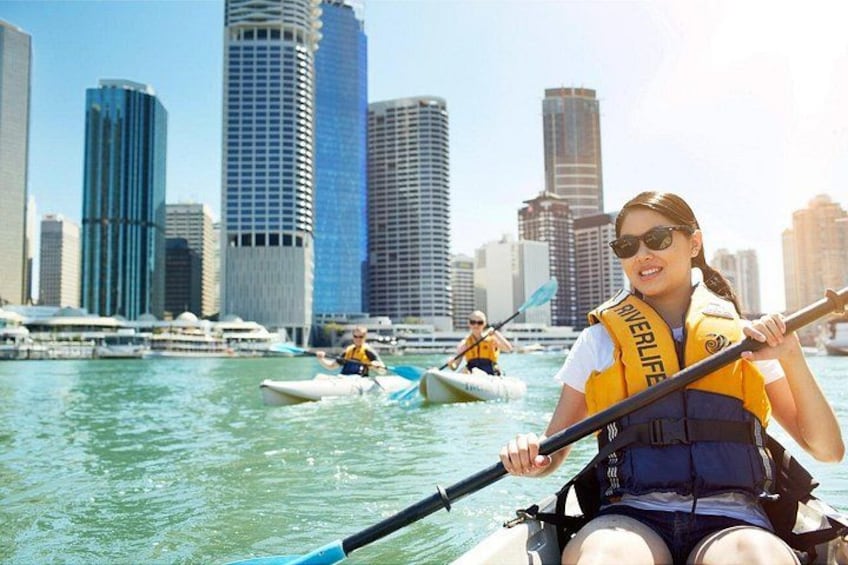 A person in a kayak with a life jacket, another person in a small boat, and a city skyline in the background. 2
