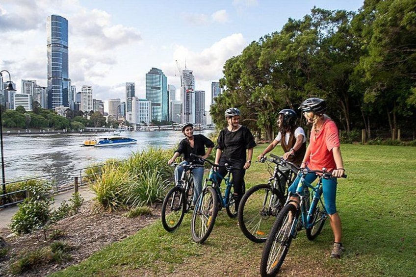 A group of people on bicycles near a river with a city skyline in the background. 4