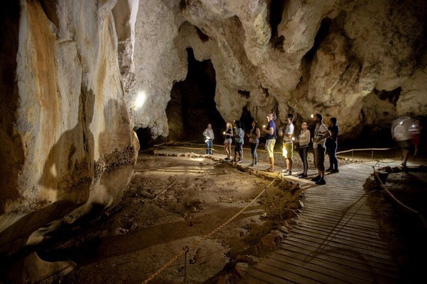 A cave with people standing on a wooden platform, examining the cave walls and floor. 2
