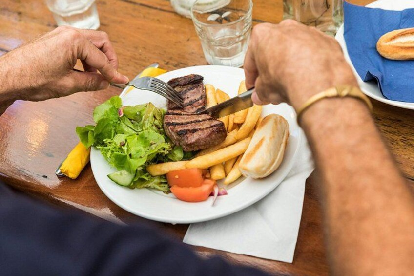 A person eating a meal consisting of grilled meat, fries, a salad, and a bun. 3