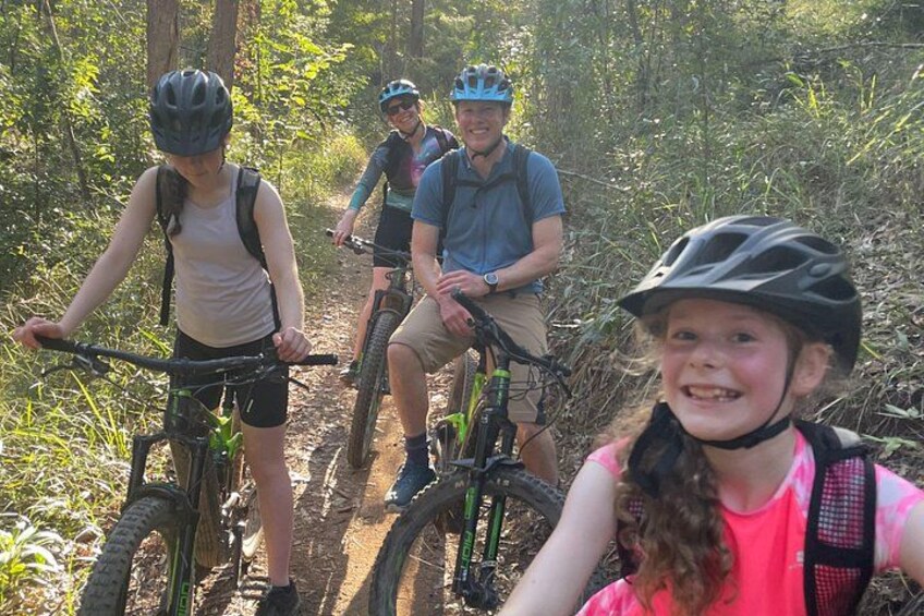 Three people on mountain bikes on a trail surrounded by trees. 5