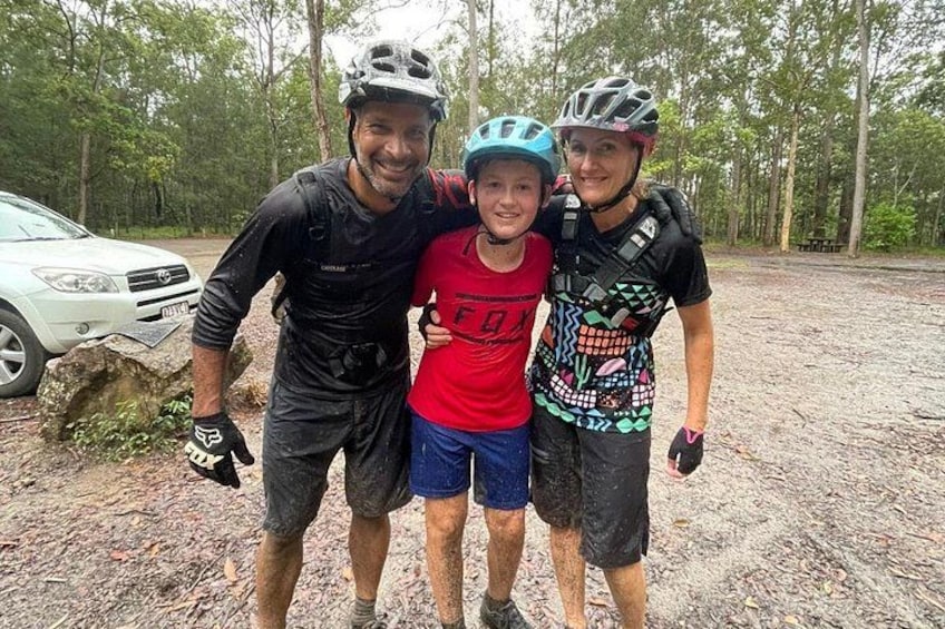 Three people wearing helmets and cycling attire, standing on a dirt path with trees in the background. 4