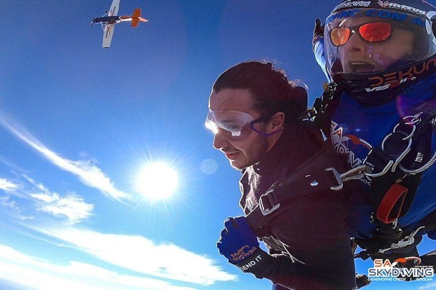 Two skydivers in freefall with a parachute and a small aircraft in the background. 2