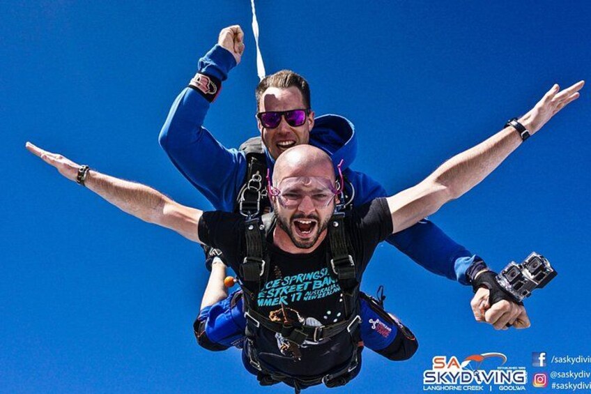 Two people skydiving with a parachute, one person is holding a camera. 1