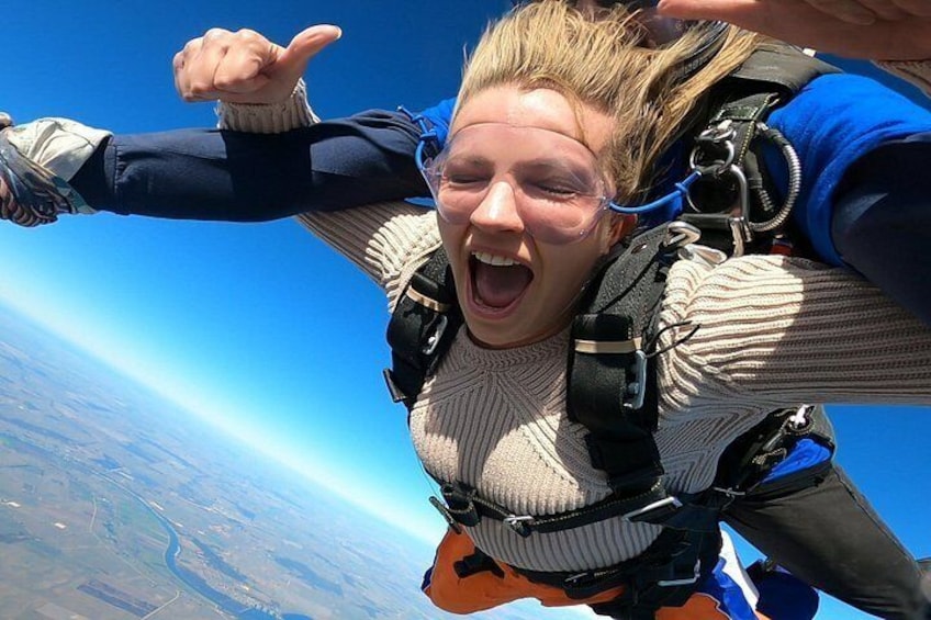 Une personne pratiquant le parachutisme, équipée d’un parachute, d’un harnais et de lunettes de protection, et bénéficiant d’une vue dégagée sur la terre en contrebas. 3