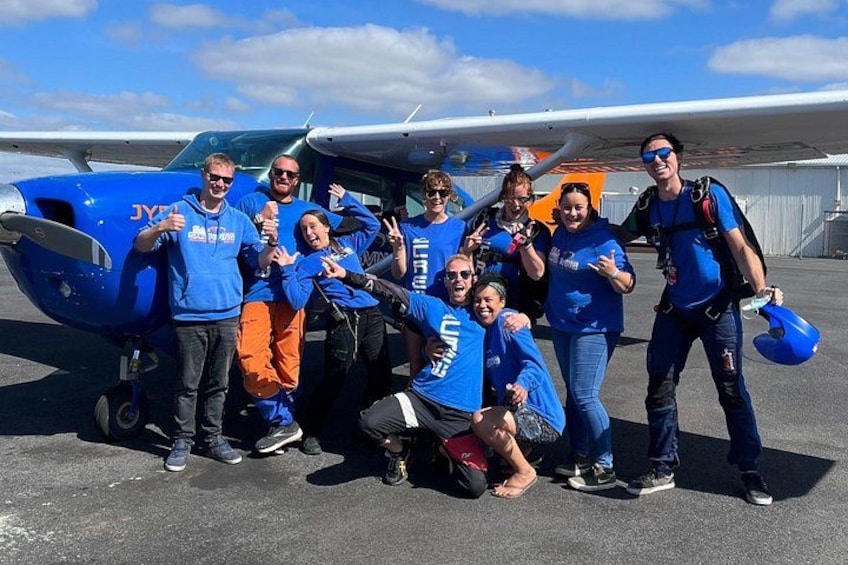 A group of people posing in front of a small blue aircraft on a tarmac. 4