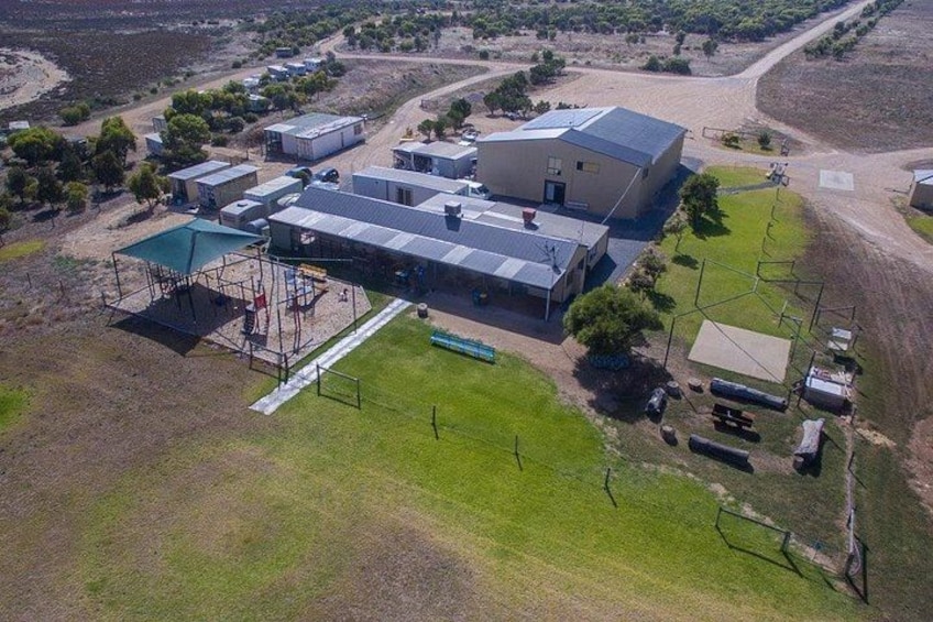 An aerial view of a large industrial facility with multiple buildings, a fenced area, and surrounding open land. 3