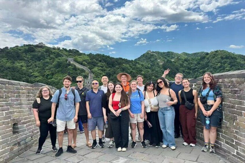 Eine Gruppe von Personen steht auf einer Steinmauer, im Hintergrund eine gebirgige Landschaft. 3