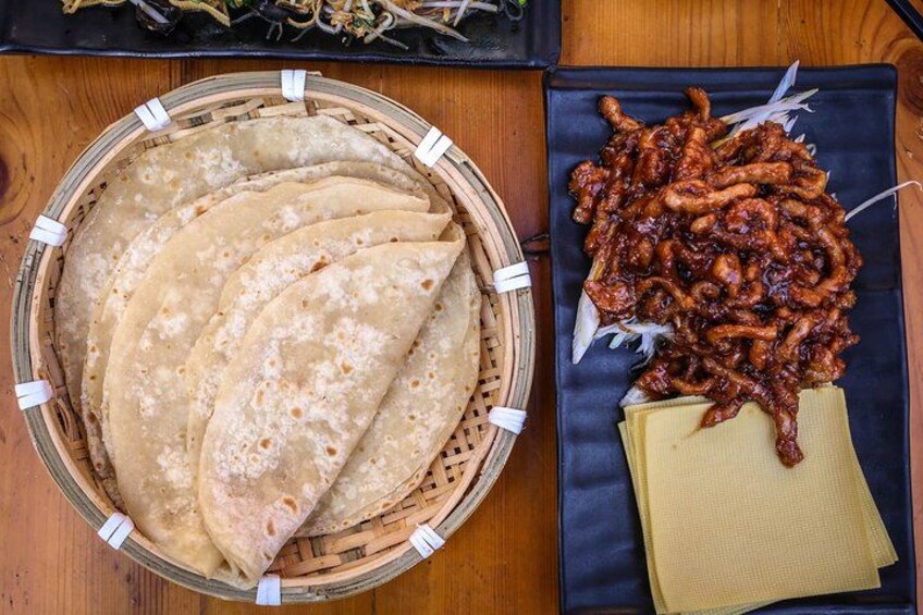 A basket of flatbreads, a plate of fried items, and a piece of yellow bread on a wooden table. 2