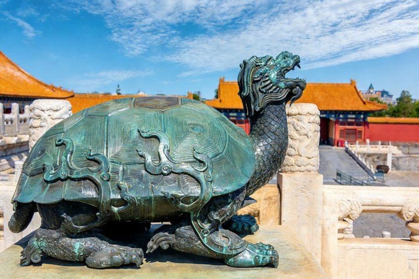 A bronze turtle statue with intricate designs, set against a traditional Chinese building with red-tiled roofs. 2