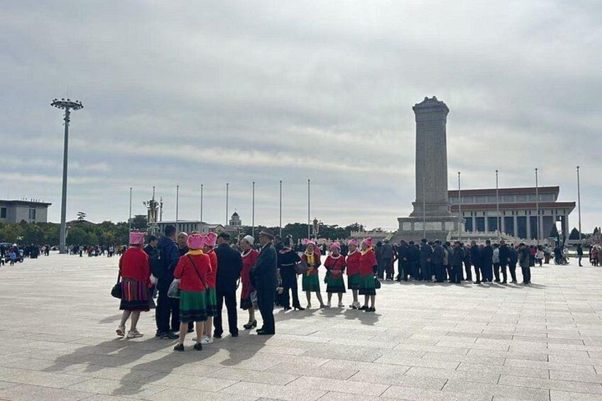 A group of people in traditional attire standing in a plaza with a tall monument in the background. 2