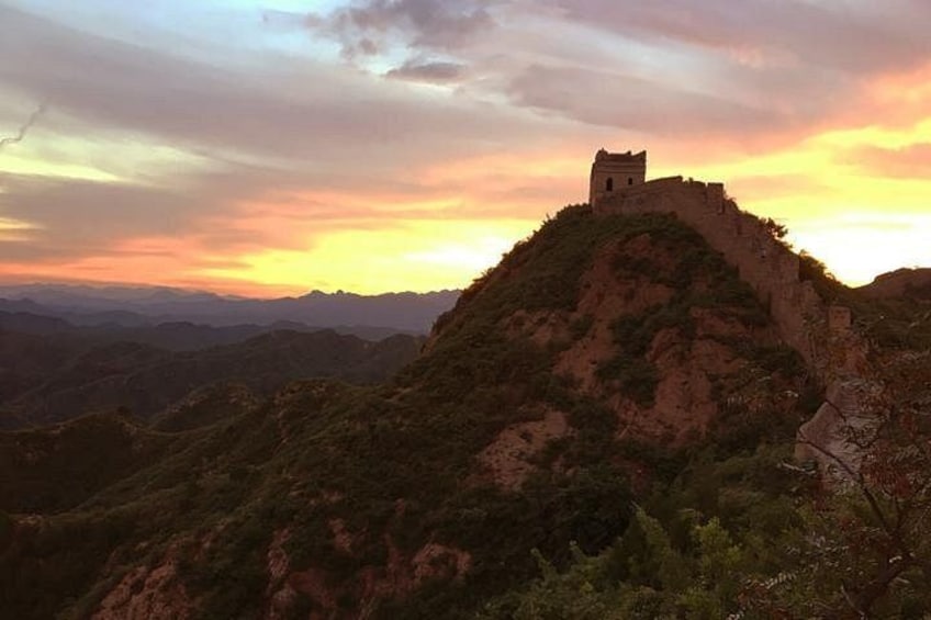 A historical wall with watchtowers, a mountainous landscape, and a sunset. 2