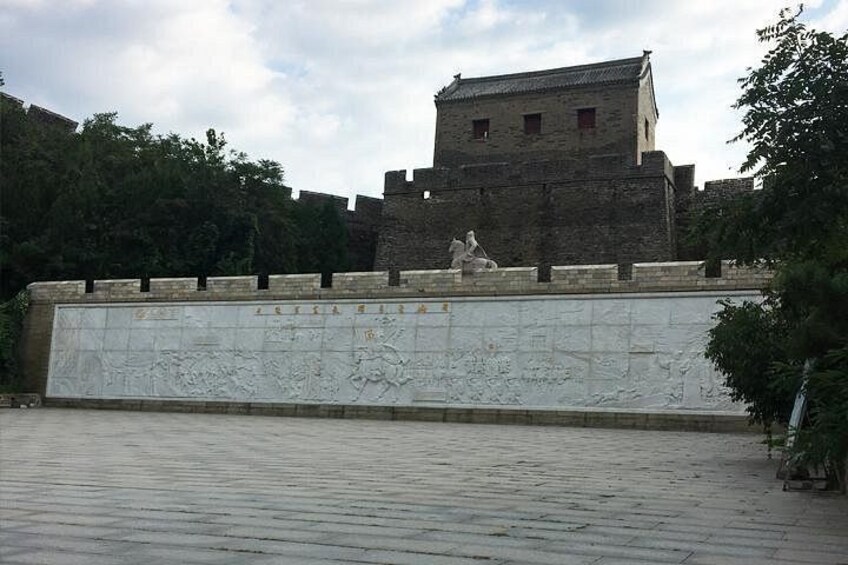 A historical stone wall with carvings, a statue, and a traditional building in the background. 3