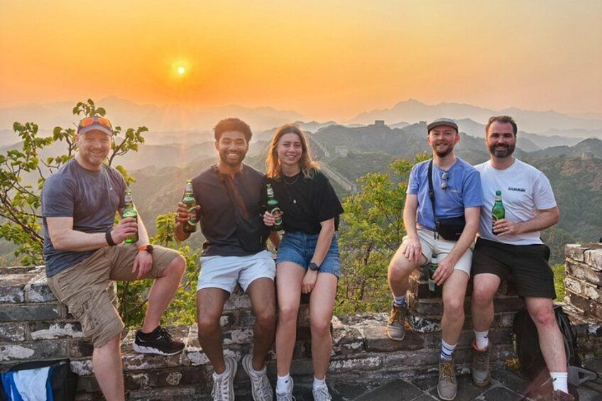 A group of people sitting on a stone wall with a sunset in the background. 4