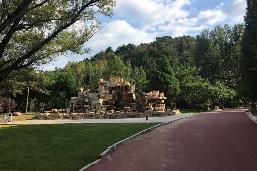 A stone ruin with a red pathway leading to it, surrounded by trees and a grassy area. 2