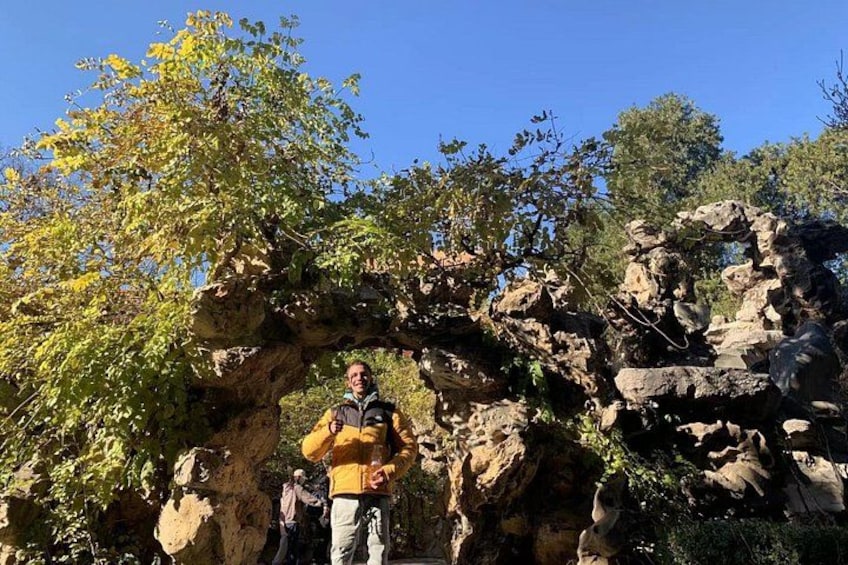 Una persona in piedi di fronte a una grande formazione rocciosa, circondata da alberi. 2
