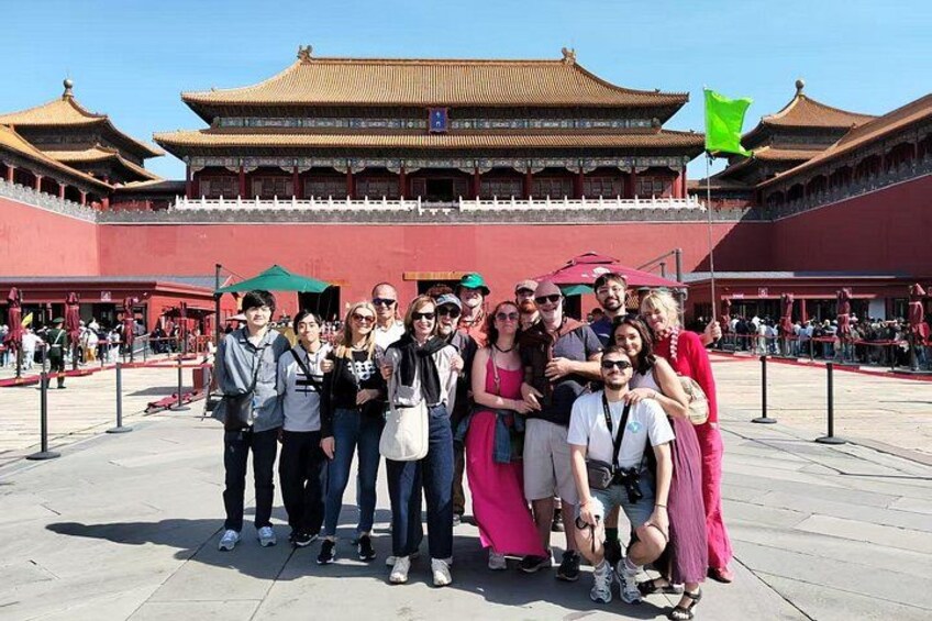 Un grupo de personas posando frente a un edificio tradicional chino con paredes rojas y techos dorados. 4