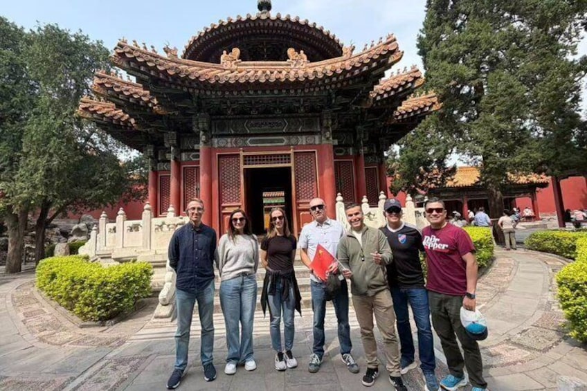 Un grupo de personas frente a una puerta tradicional china con un diseño de tejado intrincado y pilares rojos. 5