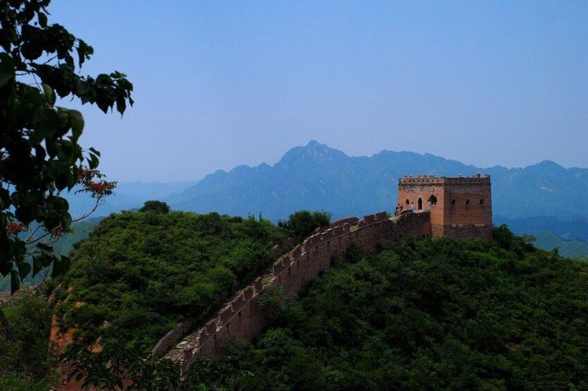 A section of the Great Wall of China with a watchtower, surrounded by lush greenery and mountains in the background. 2