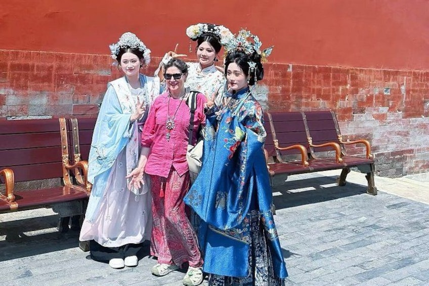 Four individuals in traditional costumes standing in front of a red wall with benches. 2