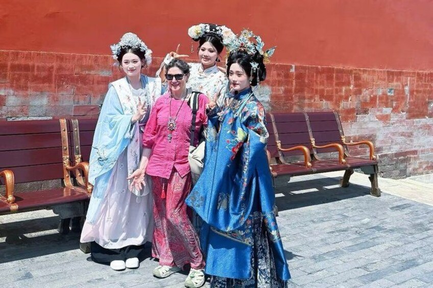 Cuatro personas vestidas con trajes típicos posando frente a un muro rojo con bancos de madera. 4