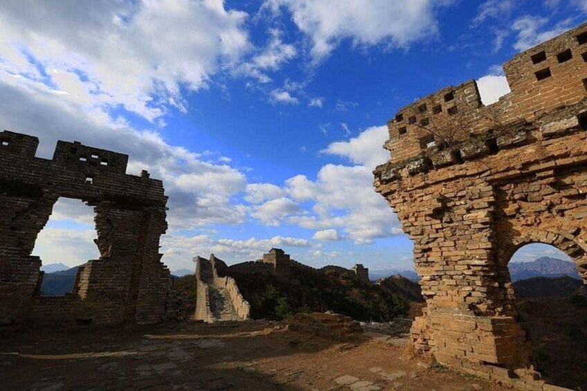 Ruinas antiguas con grandes arcos y muros de piedra, frente a un telón de fondo de montañas y un cielo parcialmente nublado. 2