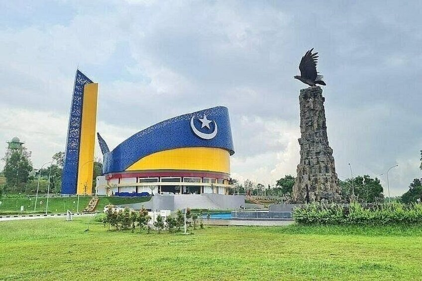A stadium with a blue and yellow roof, a tall monument, and a bird sculpture. 1