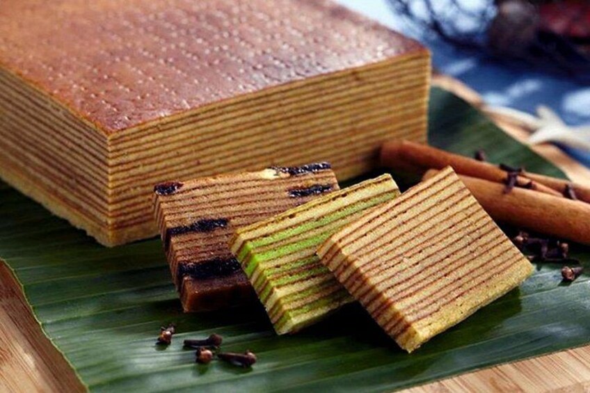 A stack of layered cakes on a green leaf, with cinnamon sticks and small brown items nearby. 3