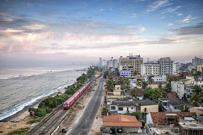 A coastal cityscape with a train on tracks, buildings, and a beach. 5