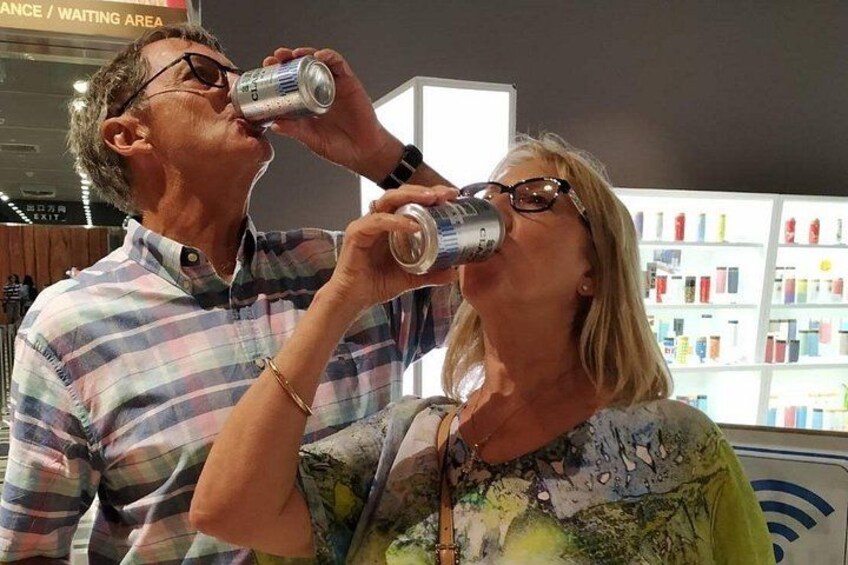 To personer drikker af dåser i en butik med hylder fyldt med produkter i baggrunden. 4