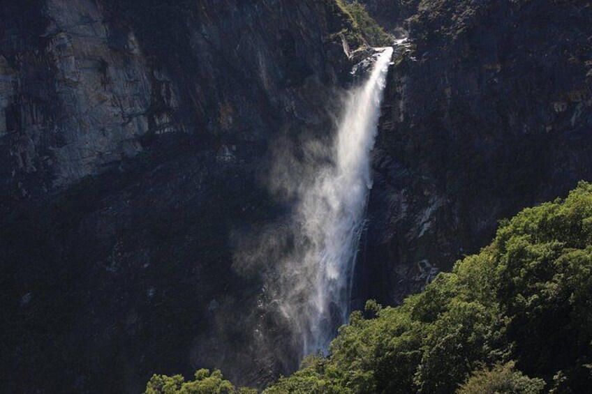 A waterfall cascading down a steep cliff surrounded by dense greenery. 2