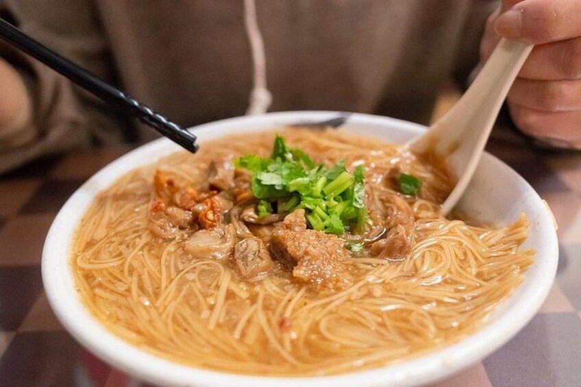 A bowl of noodle soup with meat and green garnish. 4